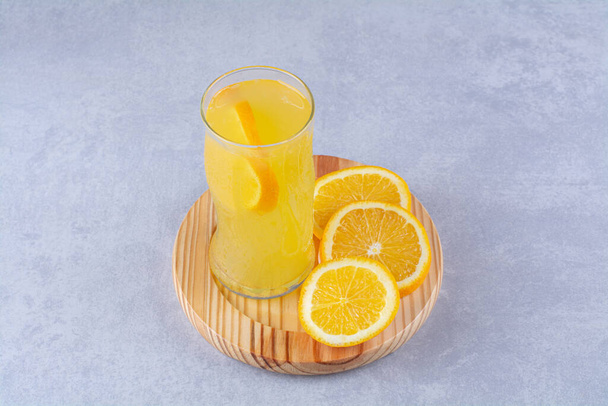Un vaso de jugo de naranja junto a rebanada de naranja en un plato de madera, sobre el fondo de mármol. Foto de alta calidad - Foto, imagen