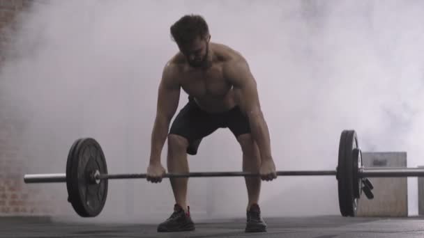 Aussperrung eines jungen, gut aussehenden kaukasischen Sportlers in Sportkleidung und Turnschuhen, der eine schwere Langhantel in der Turnhalle hochhebt und Muskeln an Beinen und Gesäß pumpt - Filmmaterial, Video