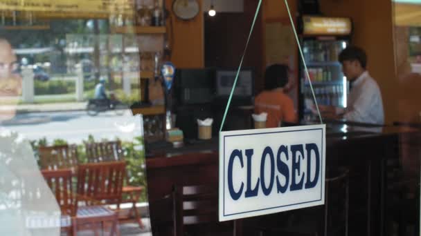 Fiatal ázsiai üzletasszony fordul tábla közel nyitott üveg bejárati ajtó a bár és üdvözlő vendégek, forgalom látható a tükörben - Felvétel, videó