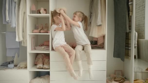Familiengarderobe. Glückliche Zwillingsschwestern im Regal im Schrank mit natürlicher Bio-Kleidung in der gemütlichen Garderobe spielen fröhlich - Filmmaterial, Video