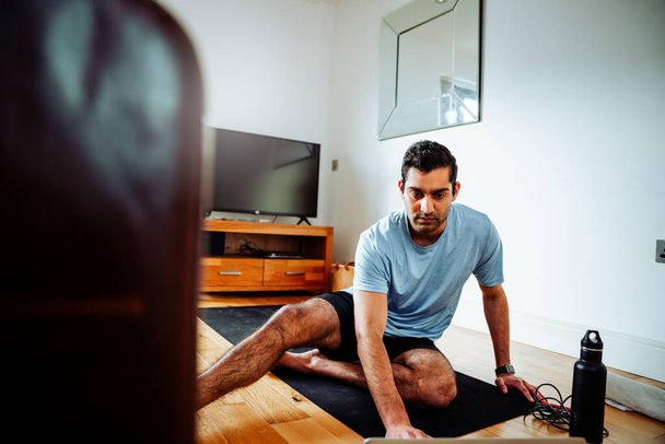 Smíšené rasy muž cvičí z domova sedí na podlaze obývacího pokoje následující program na notebooku - Fotografie, Obrázek