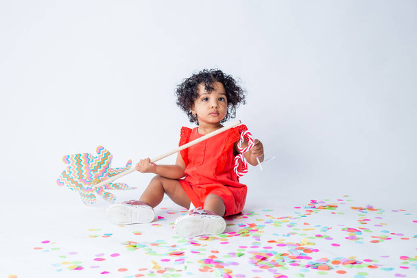 Cute little African American girl in summer clothes holding a baby windmill on a white background. the concept of summer holidays for children - Photo, Image