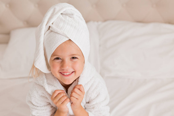 retrato de menina em roupão de banho e toalha na cabeça sorrindo para a câmera - Foto, Imagem