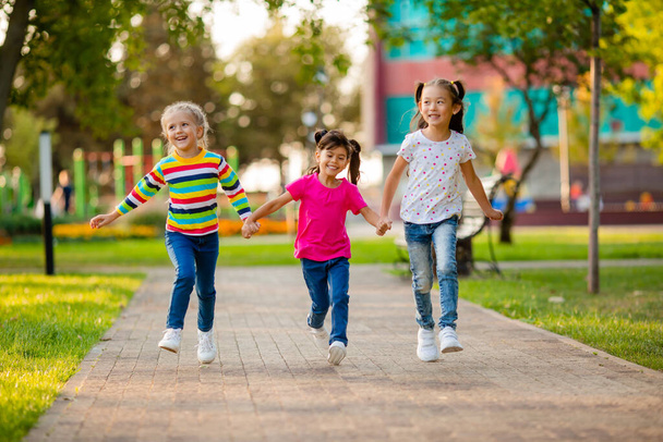 アジア系、ヨーロッパ系、インド系の3人の女の子が夏に公園で走ります - 写真・画像
