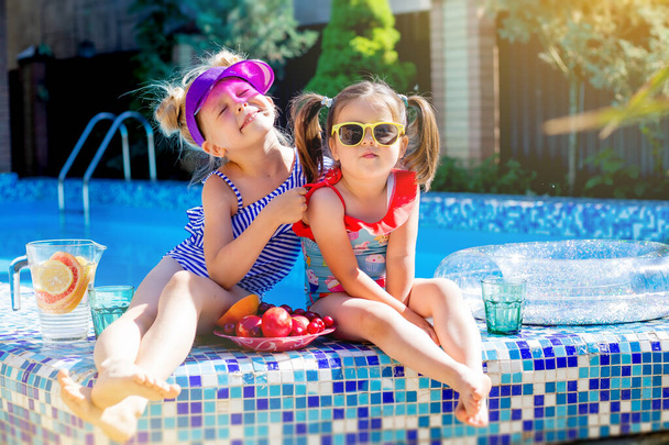 Chicas lindas sentadas cerca de la piscina, divertirse, comer frutas y beber limonada. Concepto vacaciones de verano  - Foto, imagen