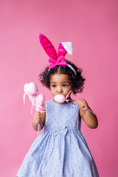 Portrét roztomilé holčičky s velikonočními králičími ušima na hlavě a velikonočními vejci. studio, růžové pozadí - Fotografie, Obrázek