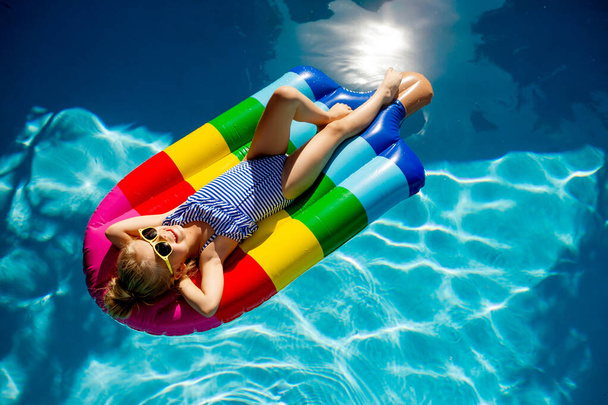 милая маленькая девочка лежит на надувном матрасе в бассейне - Фото, изображение