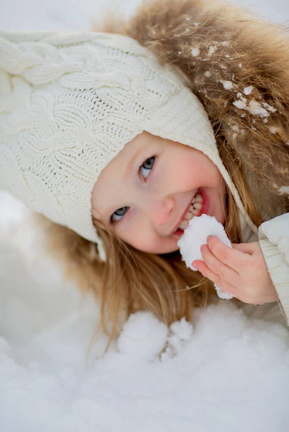klein meisje in warme kleren eten sneeuw - Foto, afbeelding