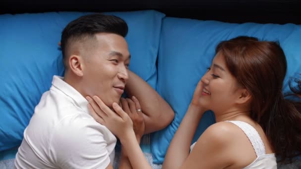Directamente encima de la vista de la pareja asiática acostada en la cama, hablando mientras la mujer toca su cara de novio - Metraje, vídeo