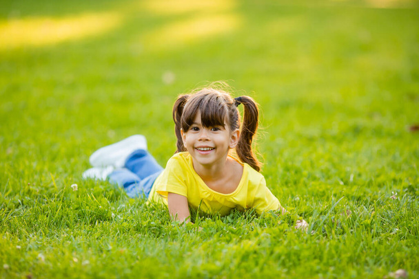 Sarı tişörtlü mutlu küçük Hintli kız yaz çimlerinde gülüyor. - Fotoğraf, Görsel