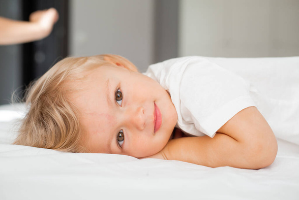 Portraitaufnahme eines lächelnden kleinen Jungen, der auf dem Bett liegt  - Foto, Bild
