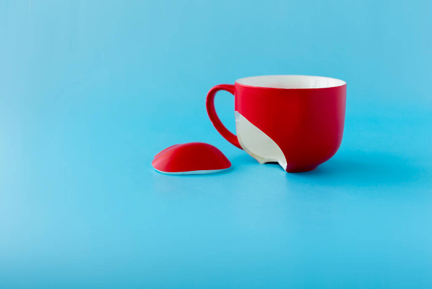 Zerbrochene rote Tasse auf blauem Hintergrund, Symbol für Scheidung, Verlust, Nahaufnahme - Foto, Bild