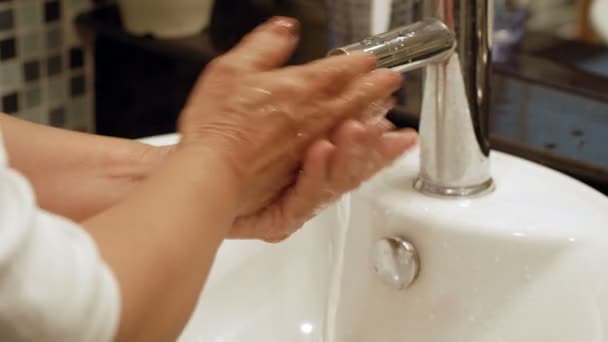 Close-up view of unrecognizable mature woman turning on faucet and washing hands with soap thoroughly over sink in bathroom - Footage, Video