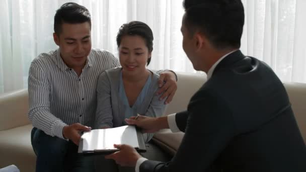 Fiatal házaspár aláírja az ingatlanvásárlási szerződést és vidáman mosolyog, miután konzultált a hivatásos brókerrel. - Felvétel, videó