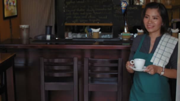 バーカウンターで働く若いアジアの女性バーのオーナーのロックダウンショット、新鮮なコーヒーのカップをもたらし、カメラで笑顔 - 映像、動画
