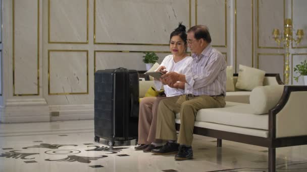 ホテルのロビーに座ってタブレットを使用している高齢者のカップルのワイドショット - 映像、動画