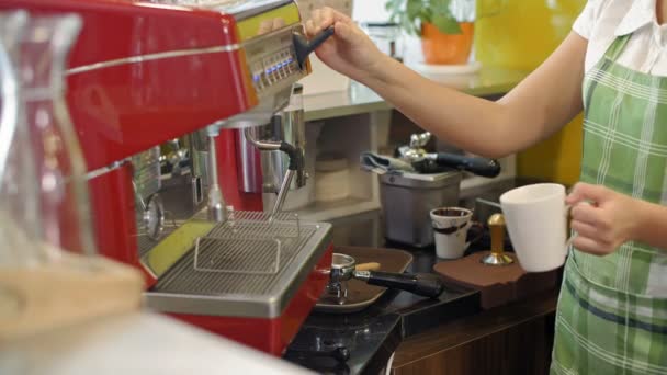 Keskikokoinen laukaus naisten barista tilalla toisessa kädessä valkoinen kuppi kahvia ja toisaalta työntämällä kahvinkeitin vipu puhdistaa sen höyryllä - Materiaali, video