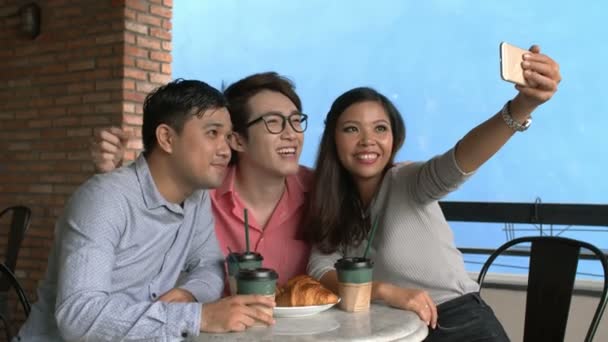 Средний снимок трех друзей, сидящих за столом в ресторане и делающих селфи на телефон - Кадры, видео