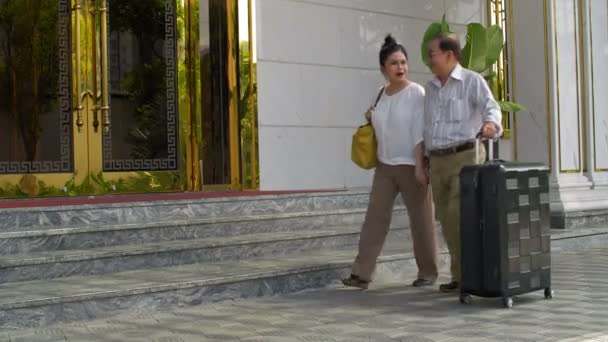 Po záběru staršího asijského muže s kufrem a jeho ženou jít do hotelu a mluvit - Záběry, video