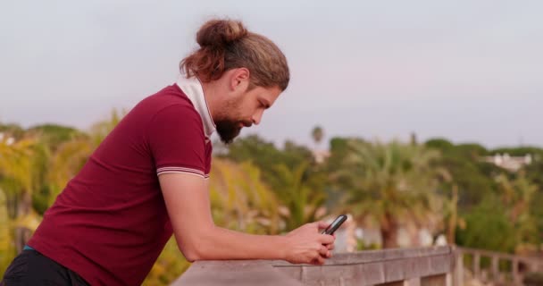 Muž komunikuje přes svůj mobilní telefon s městskou krajinou v pozadí - Záběry, video