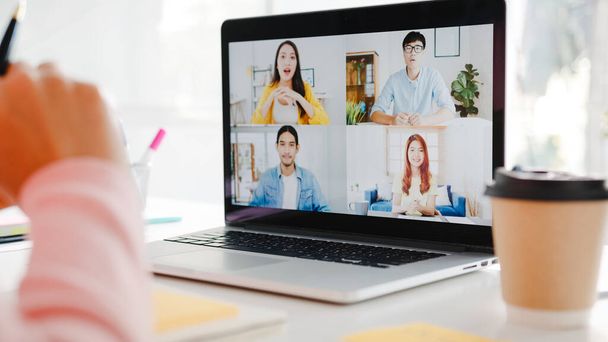 自宅のリビングルームで仕事をしながらビデオ通話会議の計画について同僚にノートパソコンの話を使用して若いアジアの実業家。自己分離、社会的距離、コロナウイルス予防のための隔離. - 写真・画像