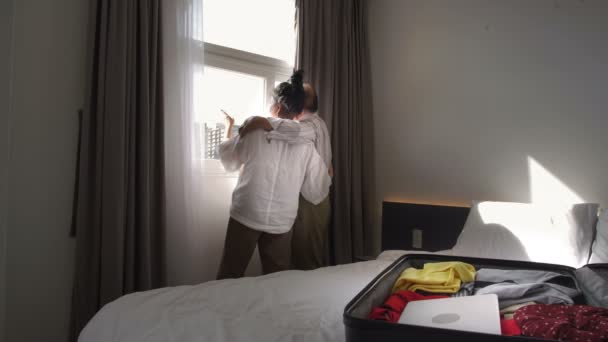 Tiro médio de homem e mulher idosos de pé juntos e olhando para fora da janela no quarto de hotel - Filmagem, Vídeo