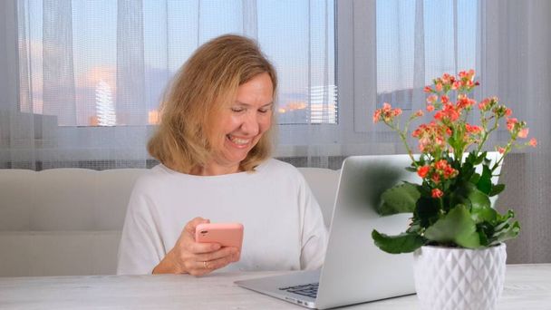 Femme utilisant un ordinateur portable et un téléphone portable à la maison, faisant des achats en ligne, travail indépendant. - Photo, image