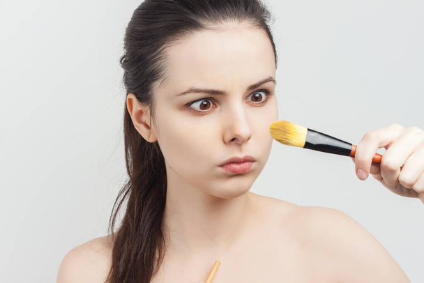 cute bare-shouldered brunette applying makeup on face cropped view - Foto, Imagem