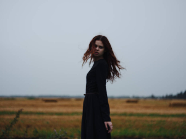 A woman in a black dress walks in the field on nature in the evening model - Zdjęcie, obraz