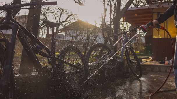 Person reinigt Mountainbikes mit Hilfe eines Wasserstrahls. Traumhaftes Panoramafoto der Fahrradreinigung, starke Sonneneinstrahlung. - Foto, Bild