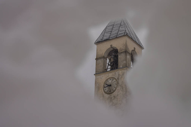 Torre de sino de uma igreja de aldeia que se esconde atrás de um buraco na neve no ambiente de inverno. Igreja de San Rocco em Vodo di Cadore - Foto, Imagem