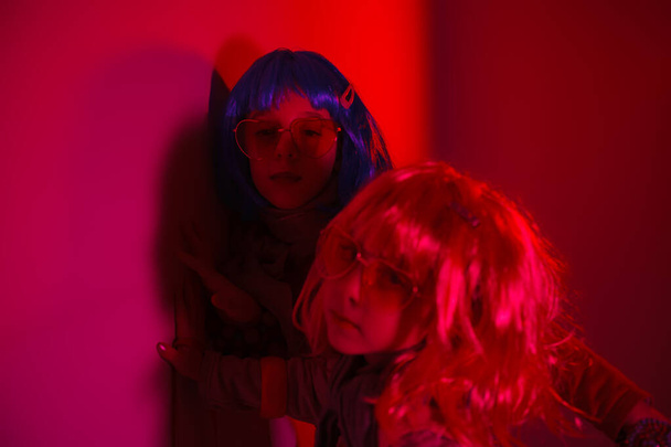 Little girls wearing a colorful wig and heart-shaped sunglasses posed for a photo shooting on the disco light background - Photo, Image