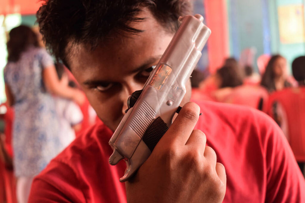 молодой парень держит перед лицом игрушечный пистолет и смотрит и улыбается - Фото, изображение