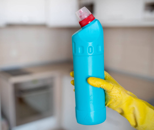 Закрыть женские руки в защитных перчатках, держа бутылку с дезинфицирующим средством перед кухонным столом - Фото, изображение