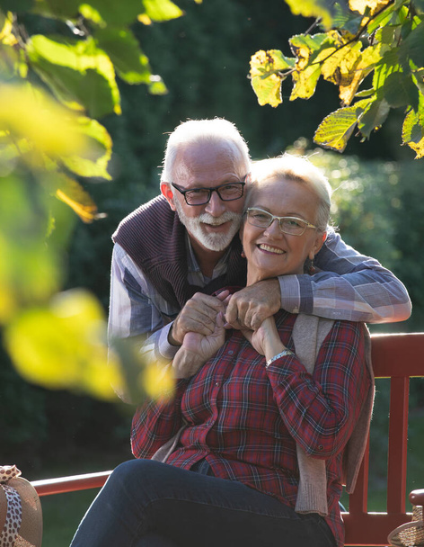 Hombre y mujer mayores abrazándose en el jardín bajo el sol de otoño - Foto, Imagen