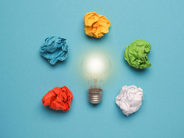 Light bulb with colorful crumpled paper balls on a blue background, great ideas concept, creativity, mindset, power - Zdjęcie, obraz