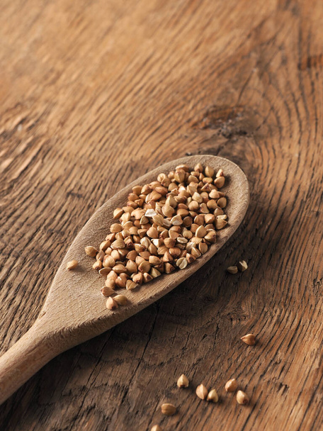 Buckwheat on a wooden spoon on a wooden kitchen table with space for text, healthy food concept - Foto, immagini
