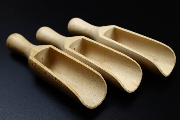 Small wooden scoops for spices on a black background - 写真・画像