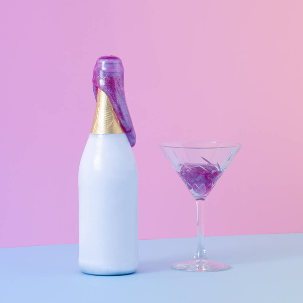 Bouteille de champagne de fête avec de la boue violette qui en sort à côté d'un verre de cristal rempli de boue. Table bleue contre mur rose. Concept créatif minimal avec lumière dégradée violette. - Photo, image