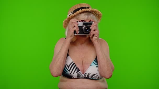 Senior γυναίκα τουρίστας φωτογράφος με μαγιό τραβώντας φωτογραφίες σε ρετρό κάμερα, χαμογελώντας στο κλειδί chroma - Πλάνα, βίντεο