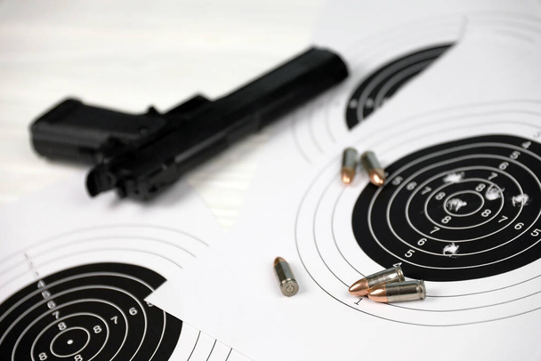 Pistole und viele Kugeln schießen Ziele auf weißem Tisch im Schießstandpolygon. Training für Ziel- und Schussgenauigkeit - Foto, Bild