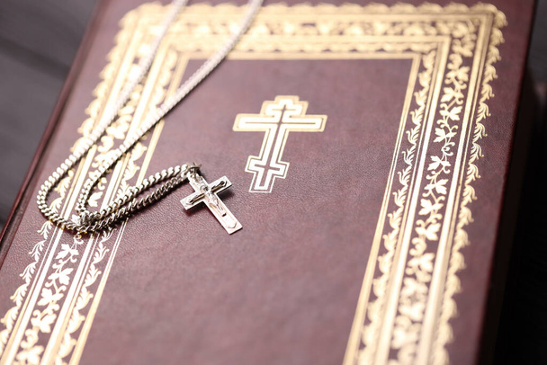 Silberhalskette mit Kruzifixkreuz auf christlichem Bibelbuch auf schwarzem Holztisch. Segen von Gott erbitten mit der Kraft der Heiligkeit, die Glück bringt und Vergebung zeigt. - Foto, Bild