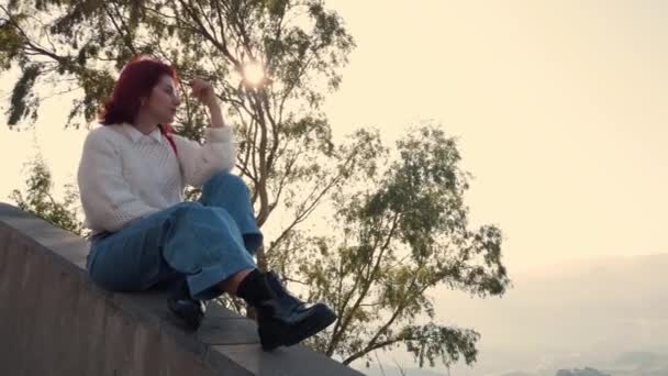 Giovane rossa si siede sul ponte di osservazione in montagna di giorno  - Filmati, video