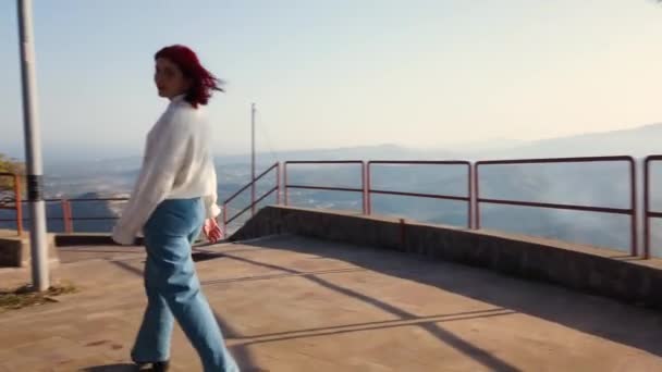 Giovane donna rossa cammina sul ponte di osservazione in montagna di giorno  - Filmati, video