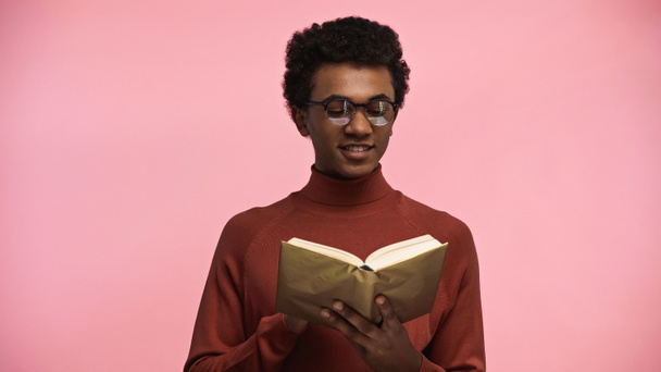 幸せなアフリカ系アメリカ人ティーンでタートルネックセーターと眼鏡読書本にピンク - 写真・画像