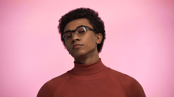 adolescent afro-américain en col roulé pull et lunettes regardant caméra isolée sur rose - Photo, image