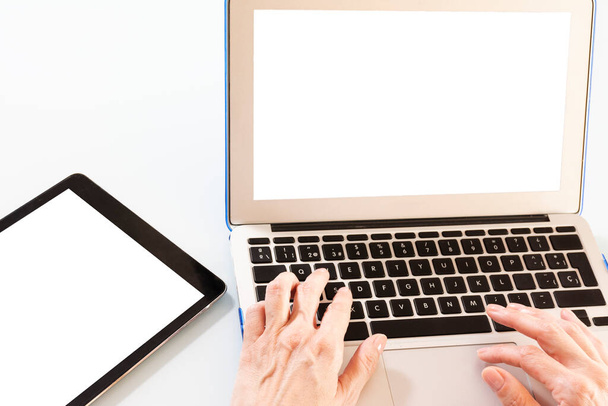 Mains de femme tapant sur un ordinateur portable à côté d'une tablette, avec des écrans blancs pour insérer des dessins ou des messages, le tout sur un fond blanc - Photo, image