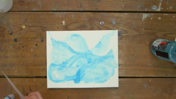 流体芸術。抽象的なカラフルな絵画。女性アーティストのトップビューは、青い抽象的な画像とキャンバスにピペットから水を注ぎ、それを配布するために絵筆を使用しています。 - 映像、動画