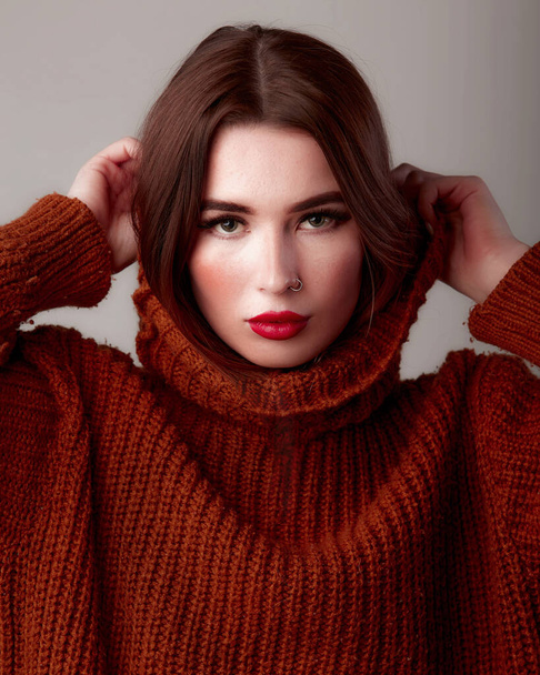 Молода красива жінка в теплий светр з горловиною. Мила жіноча модель з червоними губами. У студії на сірому фоні
 - Фото, зображення