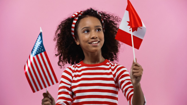 joyeuse fille afro-américaine tenant des drapeaux d'Amérique et du canada isolés en rose  - Photo, image